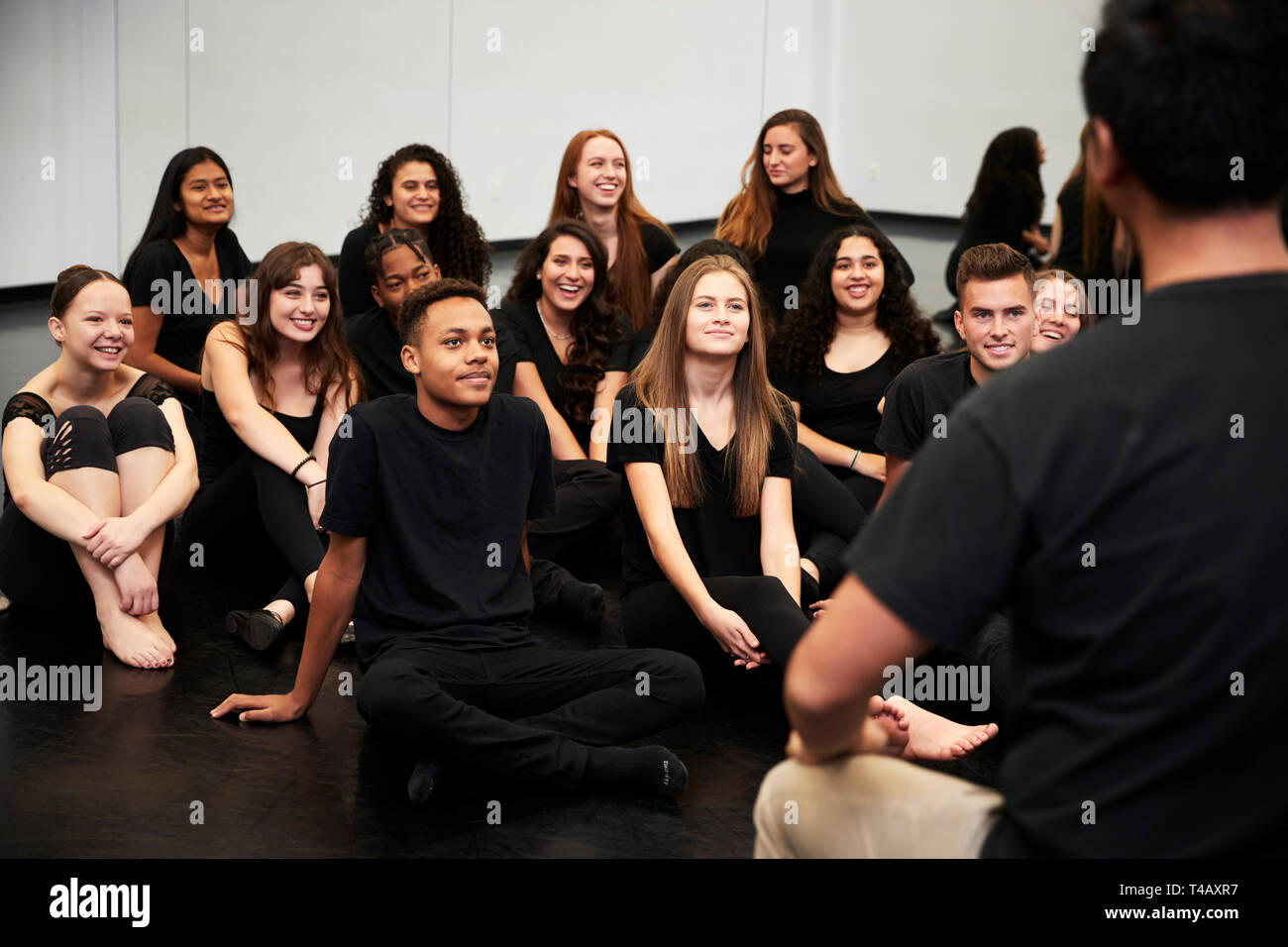 Insegnante al Performing Arts School a parlare con gli studenti seduti sul pavimento in prove di Studio Foto Stock