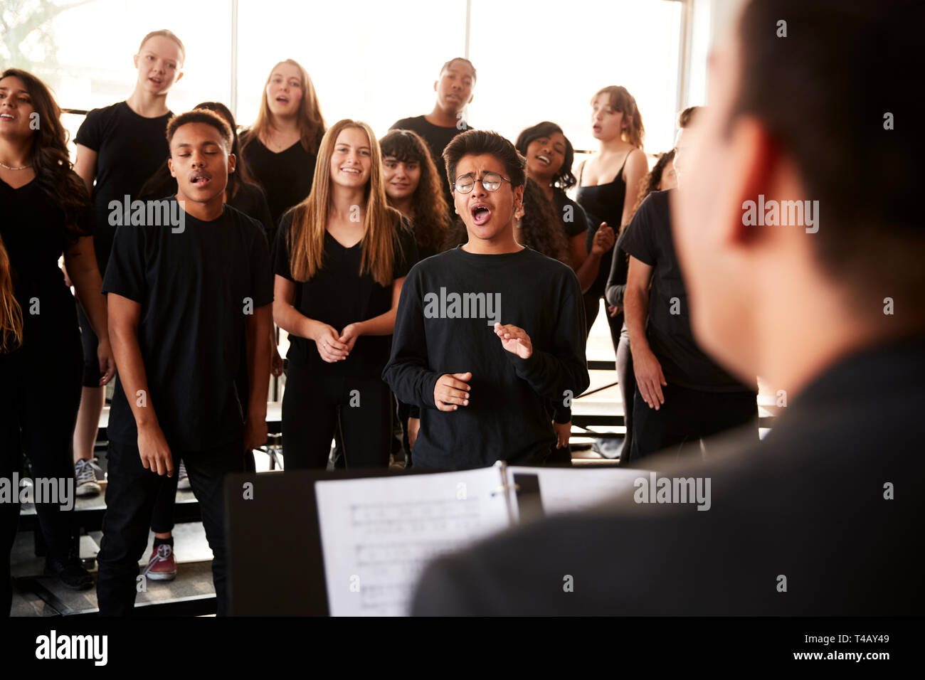 Studenti maschi e femmine a cantare in coro con insegnante a Performing Arts School Foto Stock