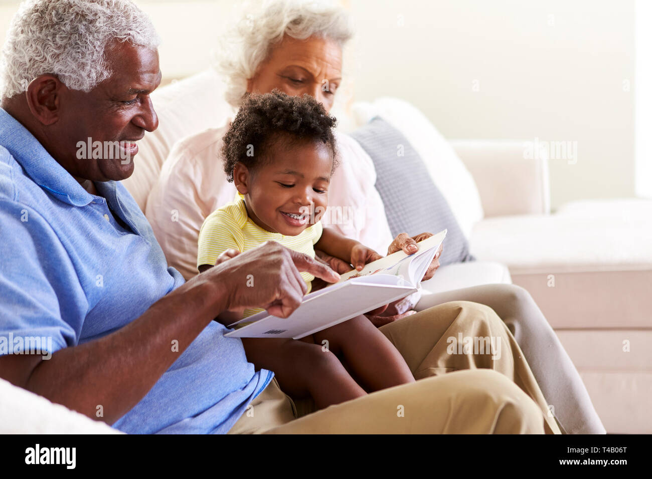 Nonni seduti sul divano di casa con il bambino nipote lettura libro insieme Foto Stock
