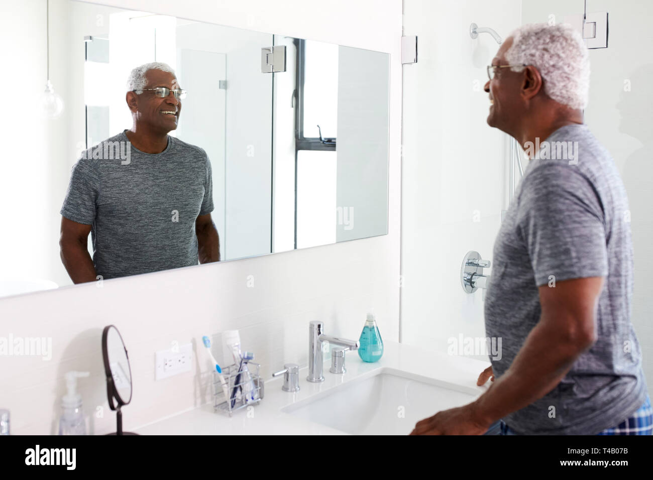 Sorridente uomo Senior guardando la riflessione nello specchio del bagno indossando pigiami Foto Stock