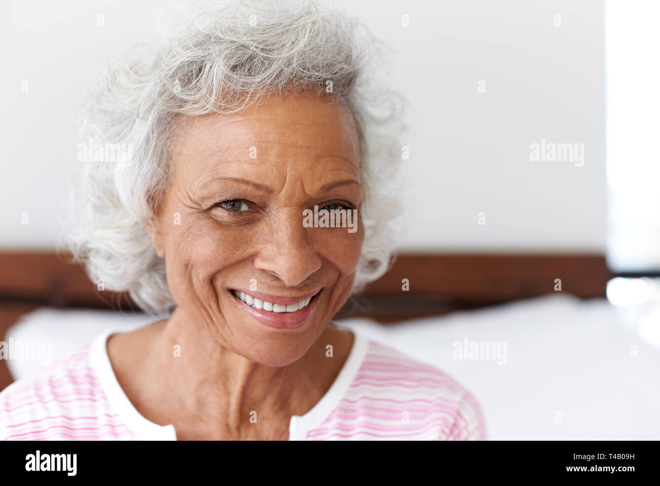 Testa e spalle Ritratto di sorridere Senior donna seduta sul letto di casa cercando positivo Foto Stock
