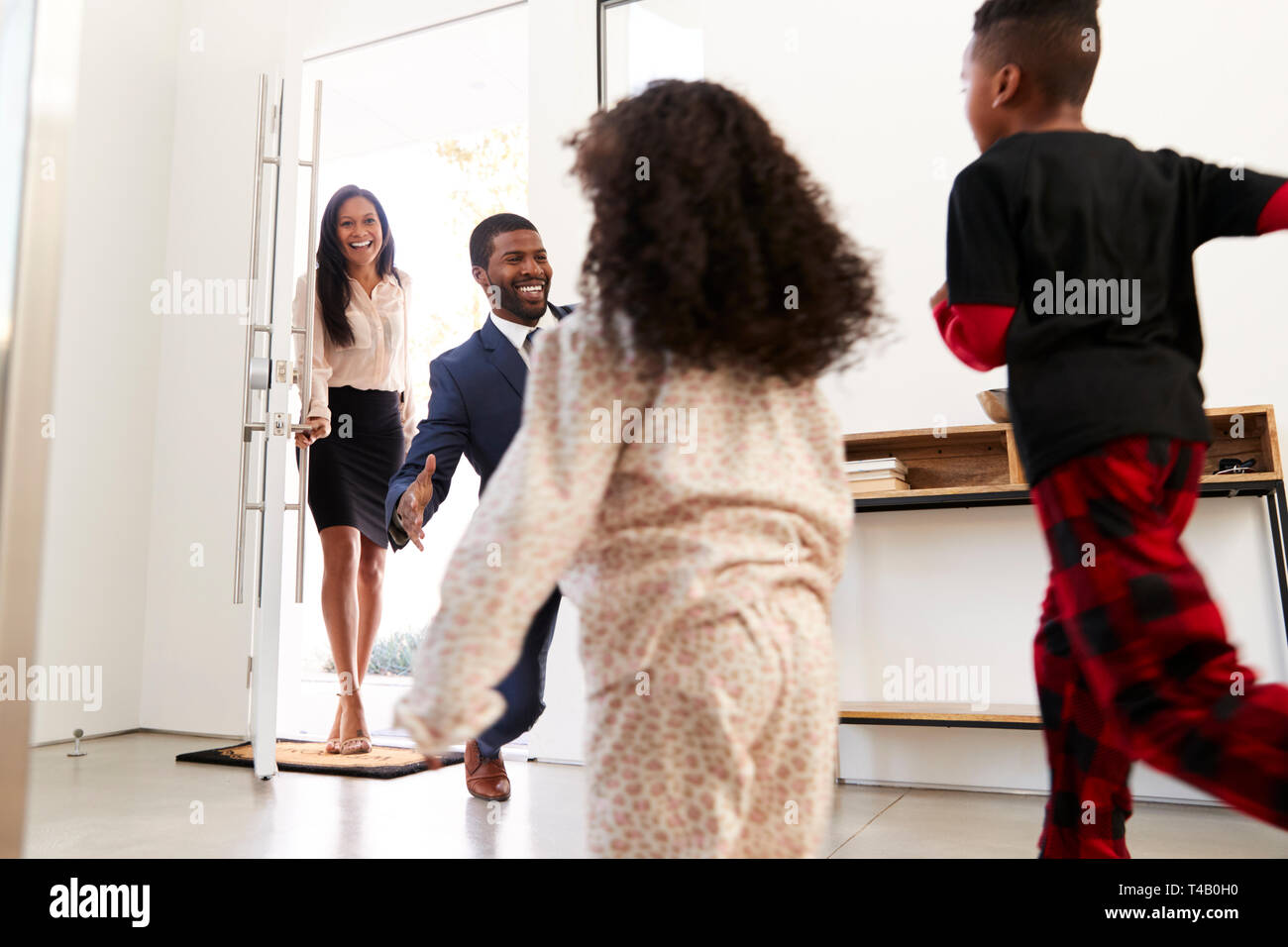 Saluto i bambini e abbracciando i genitori che lavorano come il loro ritorno a casa dal lavoro Foto Stock