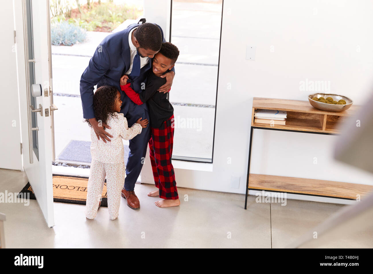 Saluto i bambini e abbracciando imprenditore lavoro padre come egli ritorna a casa dal lavoro Foto Stock