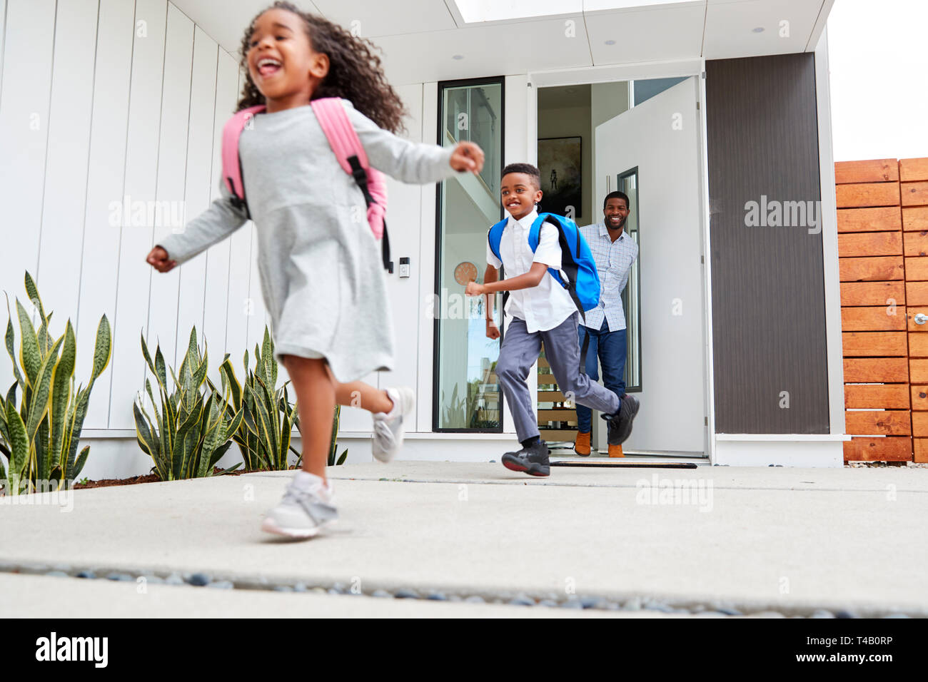 Emozionato i bambini in esecuzione fuori della porta anteriore sulla strada per la scuola guardato da padre Foto Stock