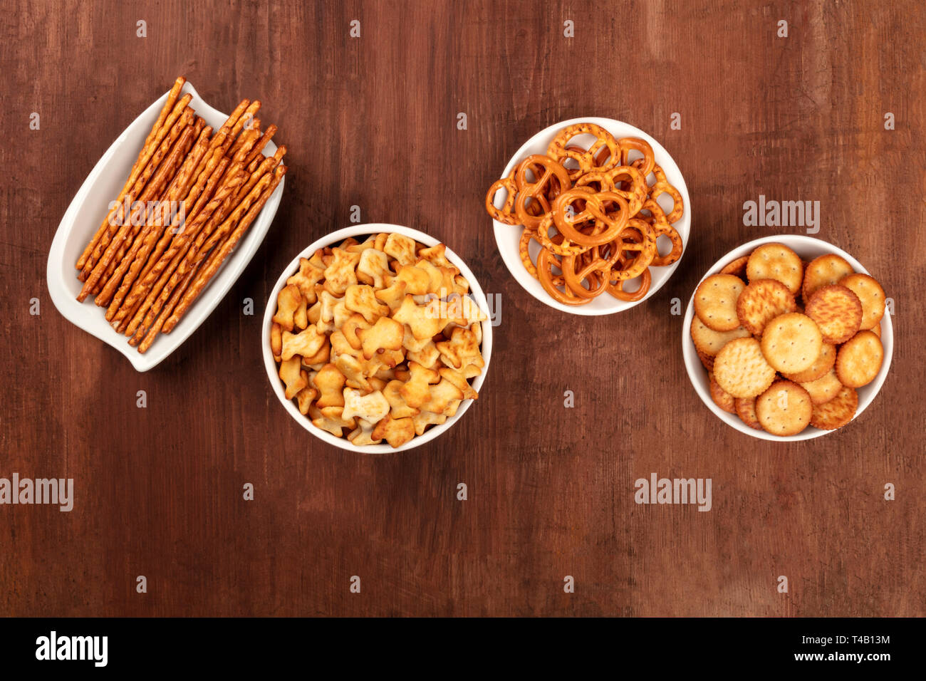 Il salato crackers, bastoncini, salatini e goldfishes, girato dalla parte superiore su di un legno scuro dello sfondo con copia spazio. Party Mix snack Foto Stock