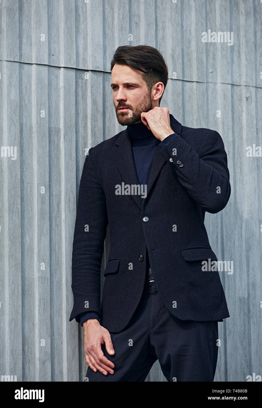 Barba di moda business stile bello modello maschile con grave aspetto concentrato in posa nello stile di abbigliamento all'esterno della parete dello sfondo. Primo piano verticale. Foto Stock