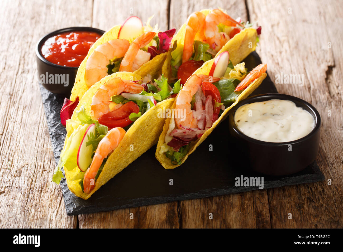 Tacos ripieni con gamberetti, verdure fresche e salse close-up sul tavolo orizzontale. Foto Stock