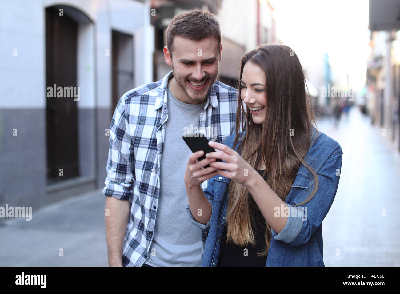 Vista anteriore verticale di una coppia felice a piedi utilizzando il cellulare in strada Foto Stock