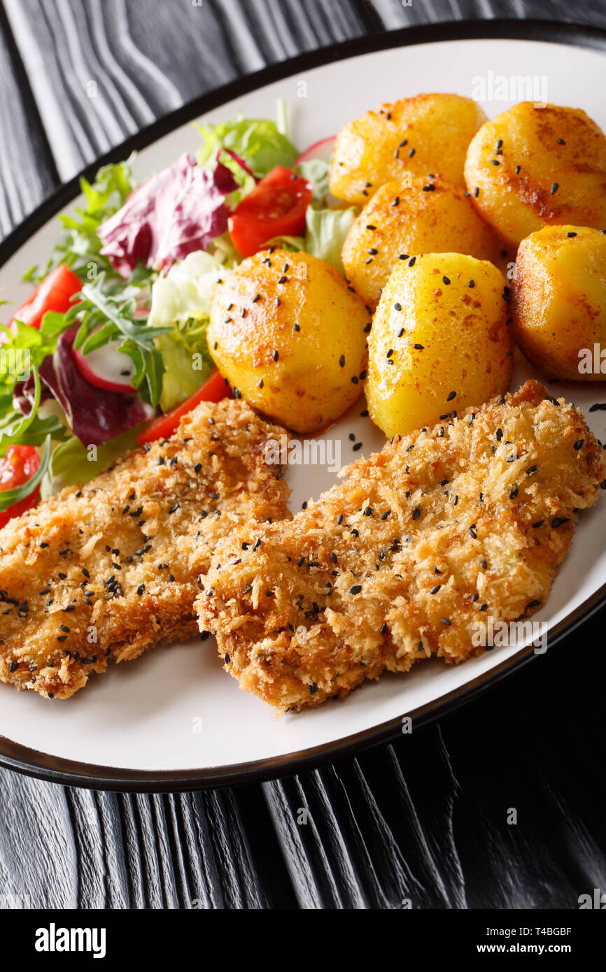 Maiale fritto bistecca con sesamo impanata con patate e insalata closeup su una piastra sul piano verticale. Foto Stock