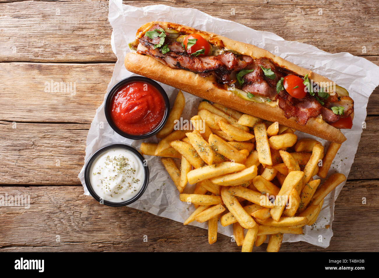Stile rustico di hot dog con pancetta e verdure servita con patatine fritte e salse close-up sul tavolo. parte superiore orizzontale vista da sopra Foto Stock