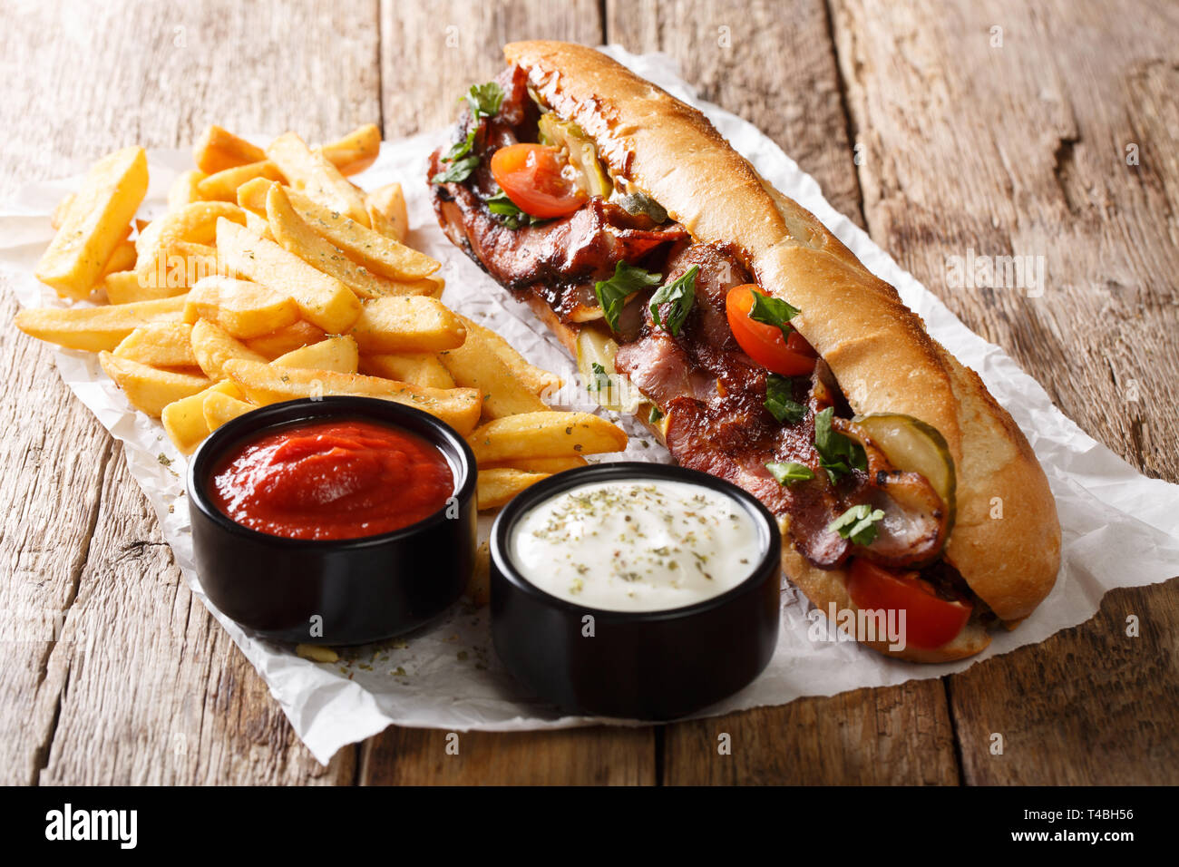 Piccante tradizionale di hot dog con pancetta fritta, verdure, patatine fritte e salse close-up sul tavolo orizzontale. Foto Stock