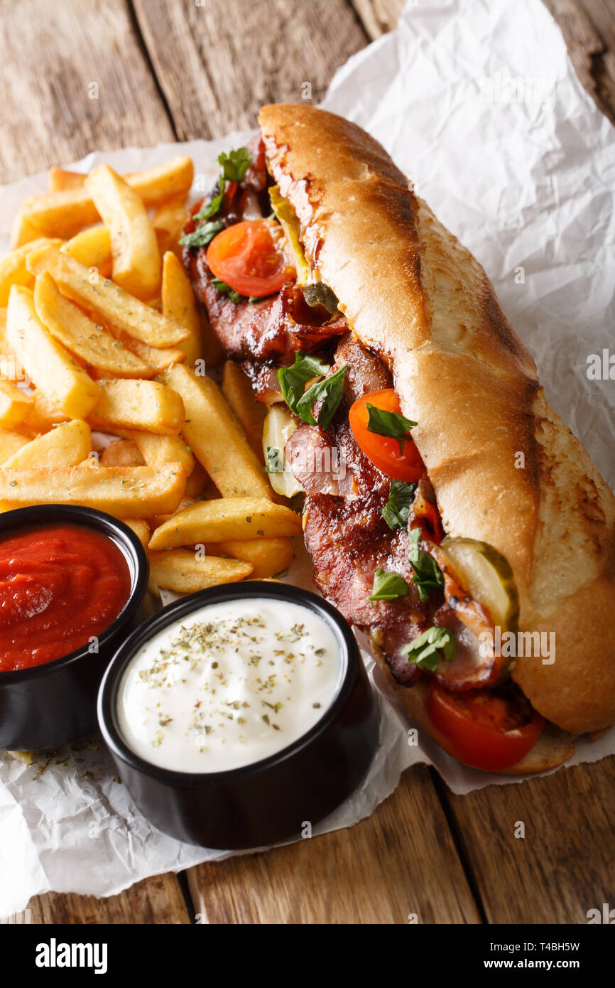 Deliziosi hot dog con pancetta e verdure servita con patatine fritte e salse close-up sul piano verticale. Foto Stock