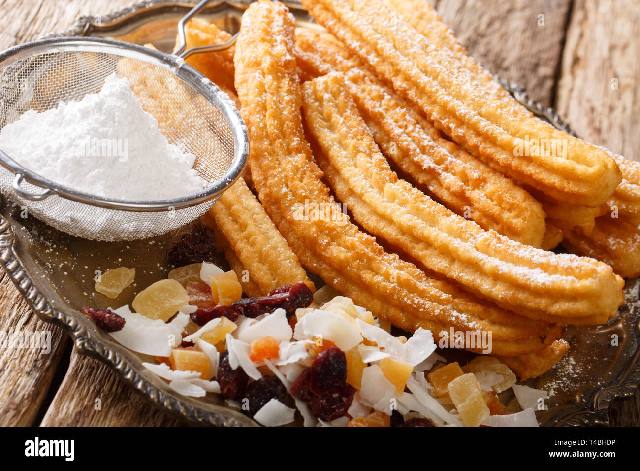 Lo spagnolo churros con zucchero a velo e frutta candita close-up su una piastra sul tavolo orizzontale. Foto Stock