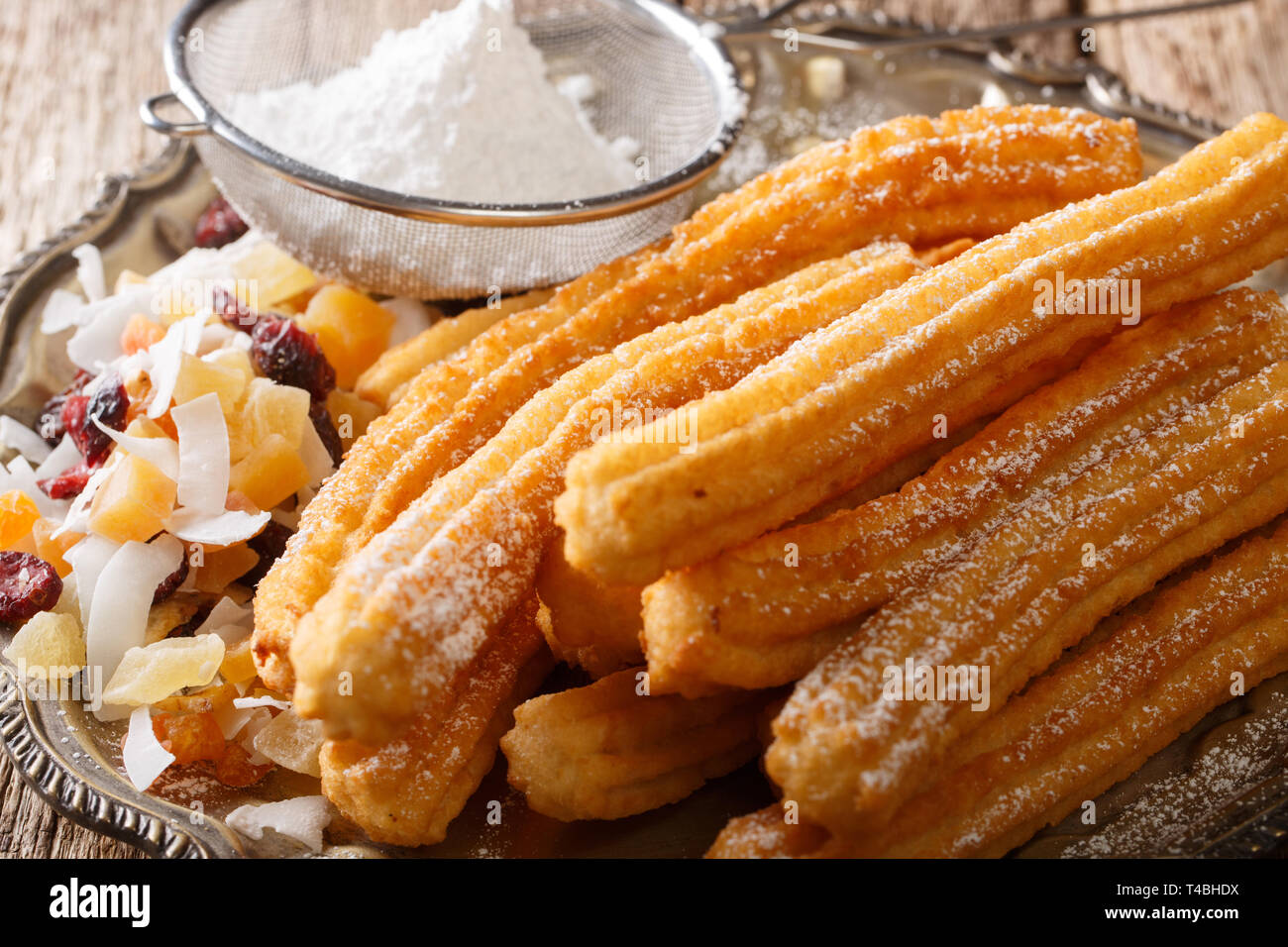 Appena fatto caldo churros con zucchero a velo e frutta candita vicino sul tavolo orizzontale. Foto Stock