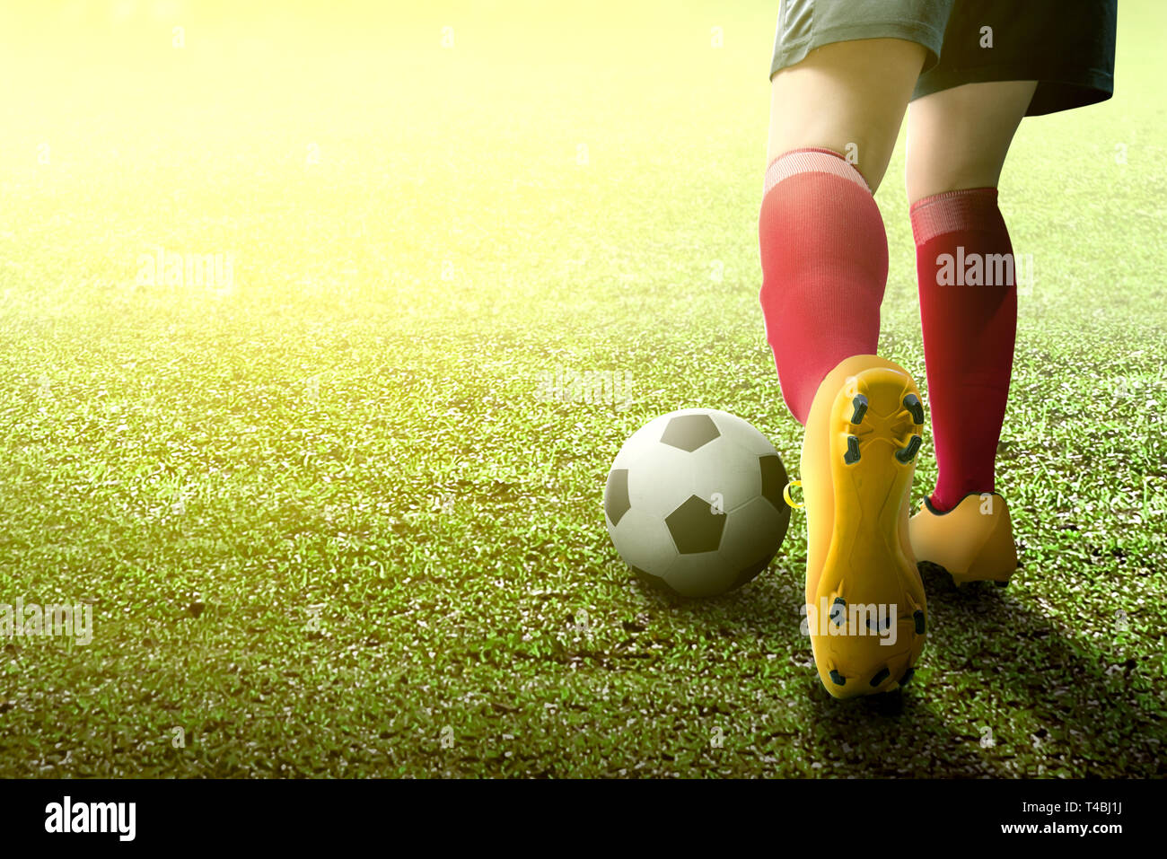 Vista posteriore del giocatore di football donna in maglia arancione calciare la palla sul campo verde Foto Stock