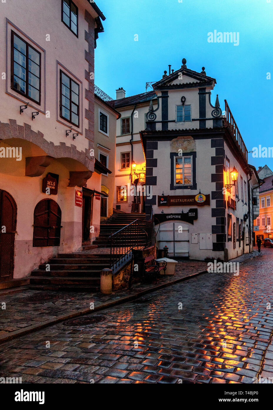 Passi conducono un passaggio da un ristorante dalla wet strada acciottolata a Cesky Krumlov al crepuscolo Foto Stock