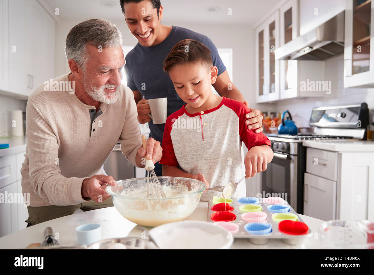 Papà guardando il suo figlio a fare torte con il nonno al tavolo della cucina, close up Foto Stock