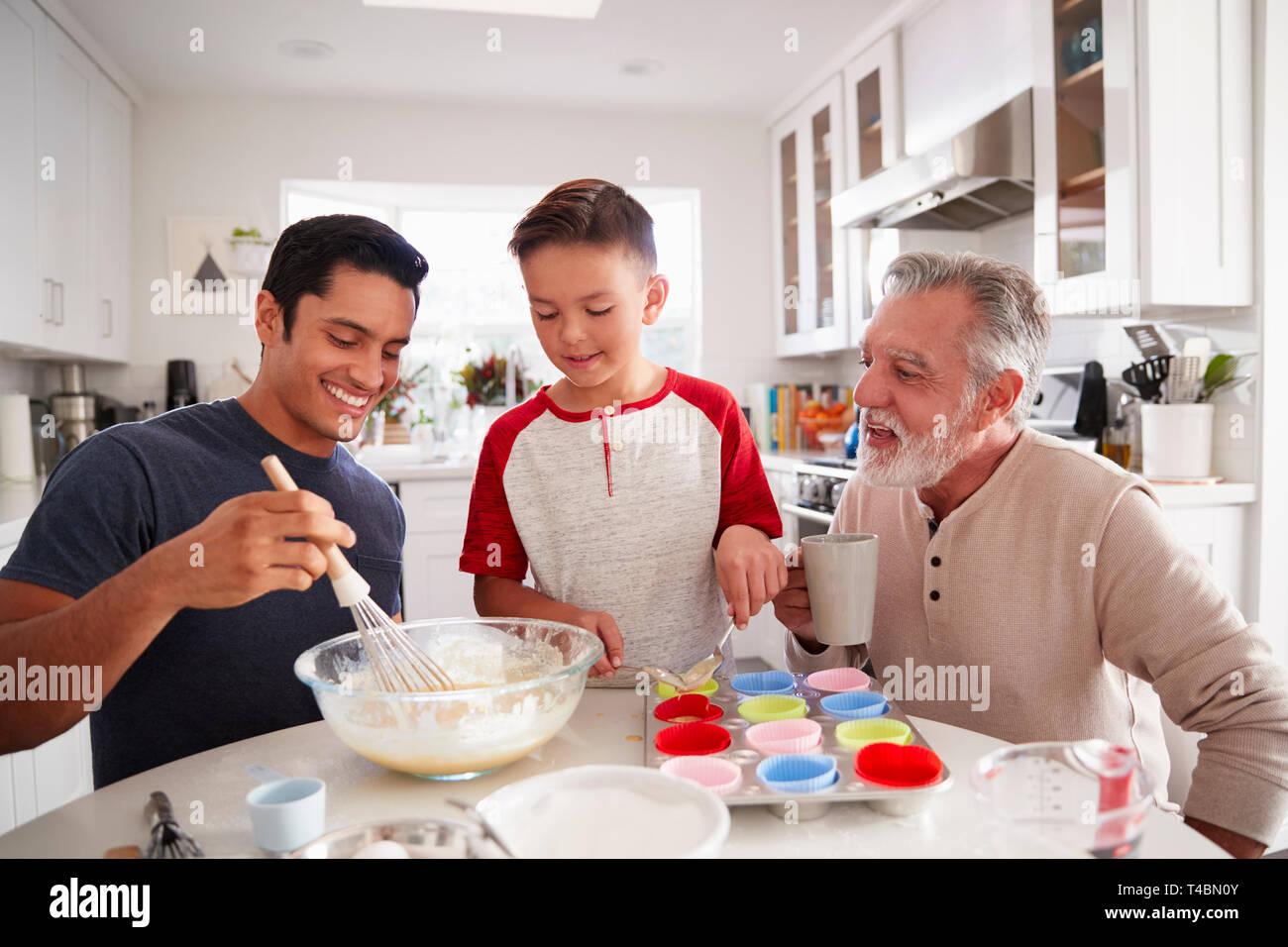 Tre generazioni maschili della famiglia preparare torte insieme al tavolo della cucina, close up Foto Stock