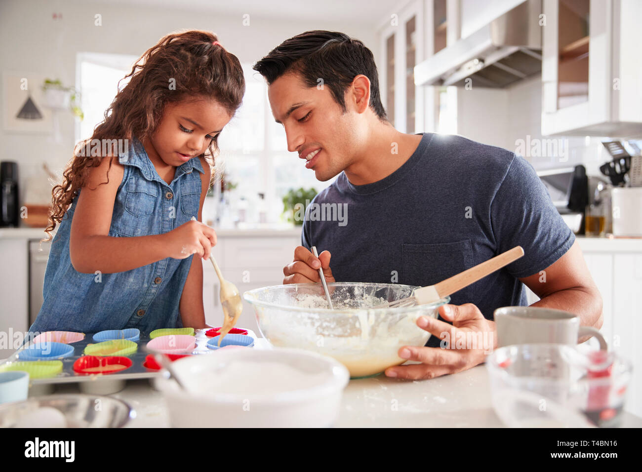 Ragazza giovane permanente al tavolo della cucina a fare torte con suo padre, il riempimento di forme di torta, close up Foto Stock