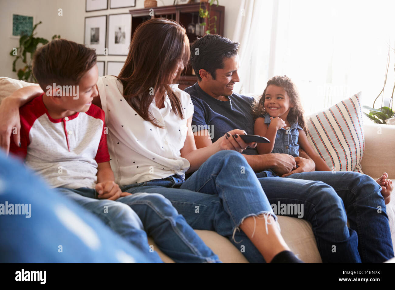 Giovane famiglia ispanica seduti sul divano di casa a guardare la TV, guardando ogni altro ravvicinato Foto Stock