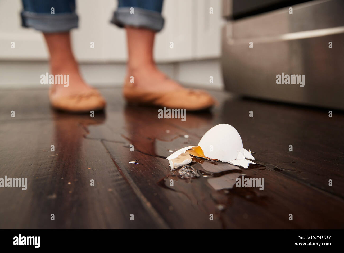 Un uovo rotto sul pavimento della cucina dopo un piccolo incidente di cottura, piedi in background, angolo basso Foto Stock