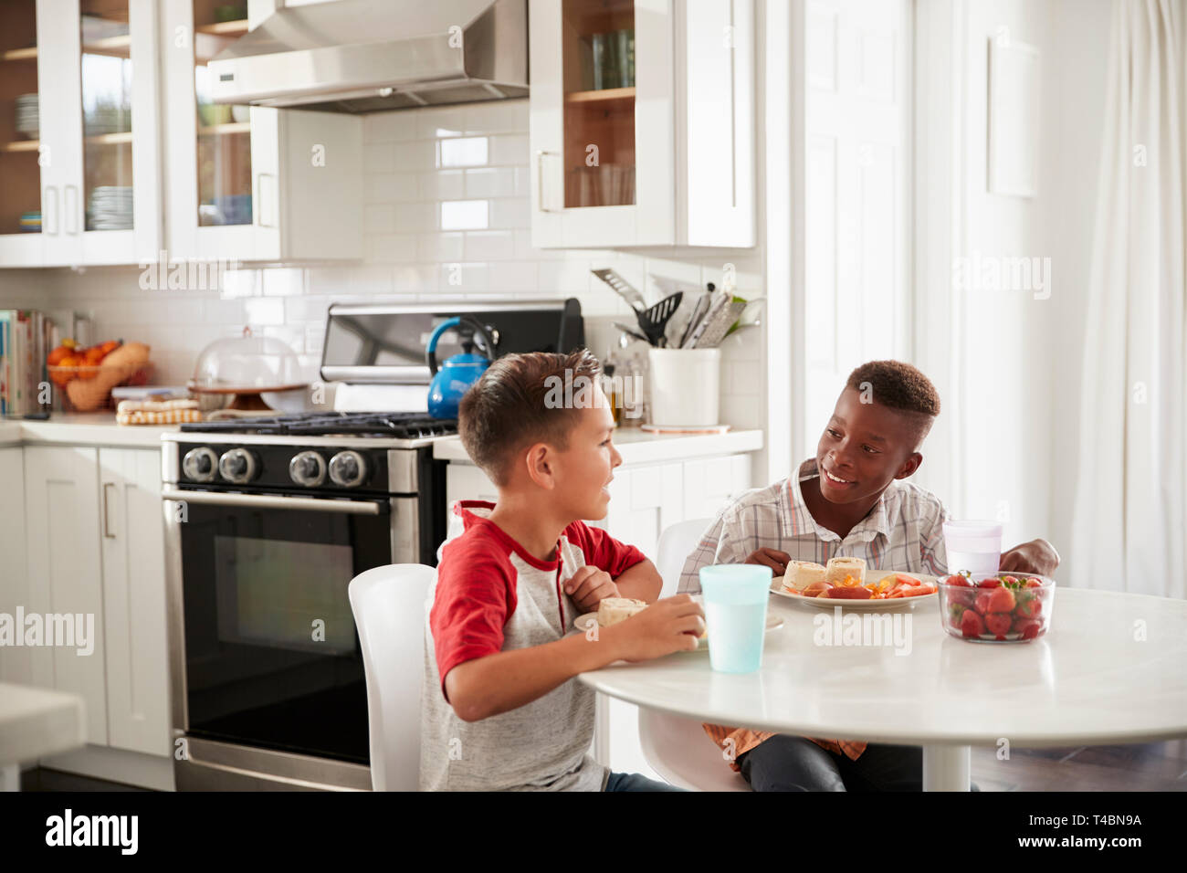 Due pre-teen maschio gli amici siedono a parlare in cucina durante un playdate ad un ragazzo in casa Foto Stock