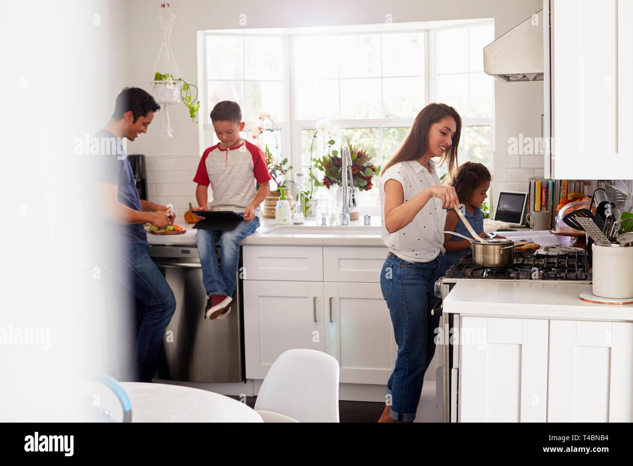 Madre e figlia giovane prepara il cibo in cottura in cucina, pre-teen figlio e papà in background Foto Stock