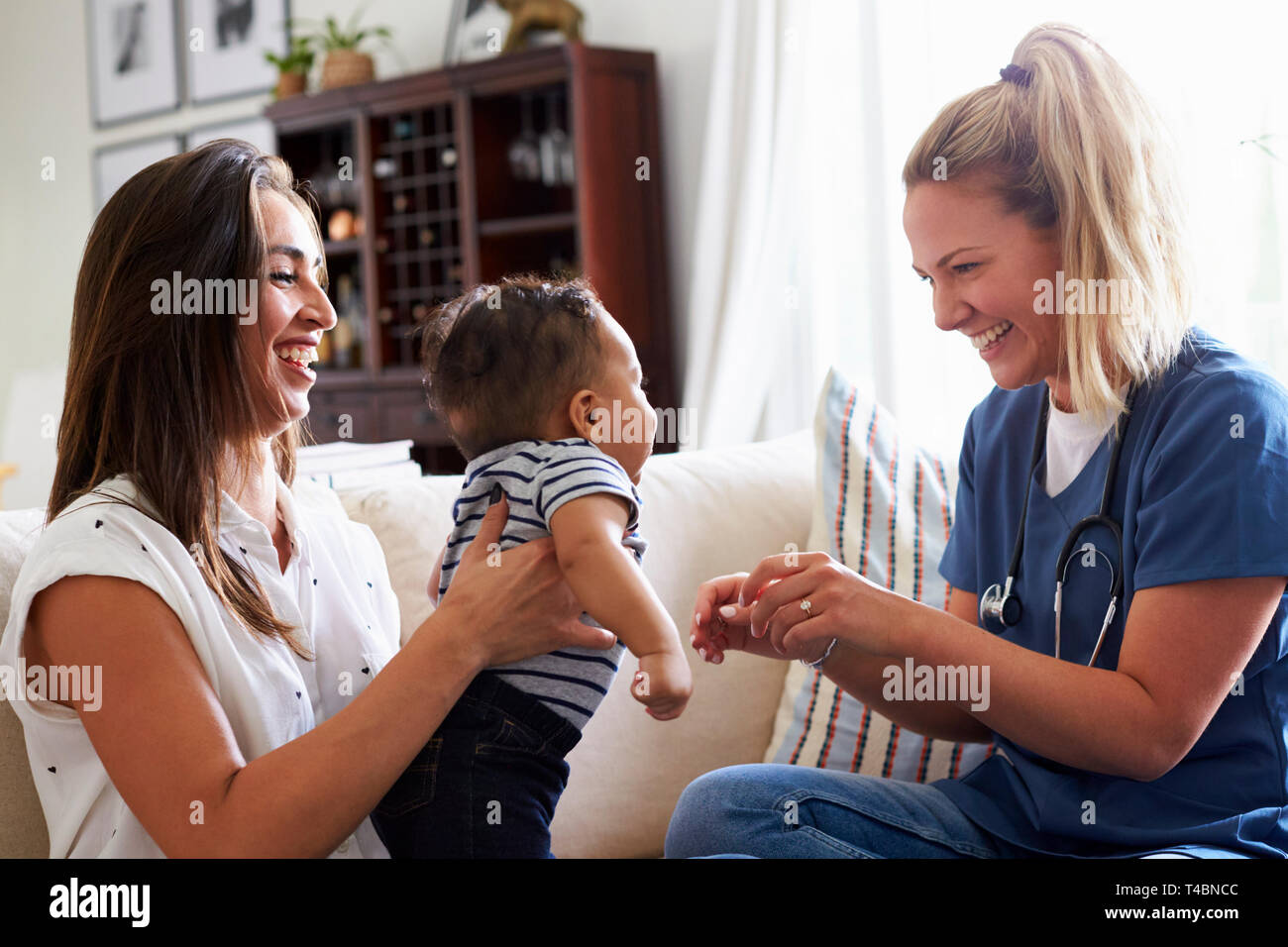 Femmina lavoratore del settore sanitario in visita a una giovane mamma e suo figlio bambino a casa Foto Stock