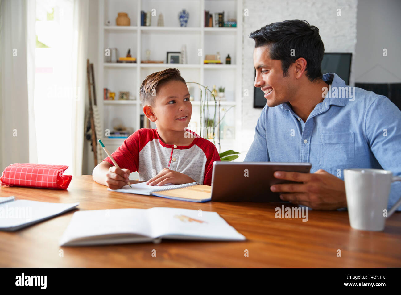 Ispanico pre-teen boy seduta a tavola che lavora con il suo home la scuola tutor, sorridente ad ogni altro Foto Stock