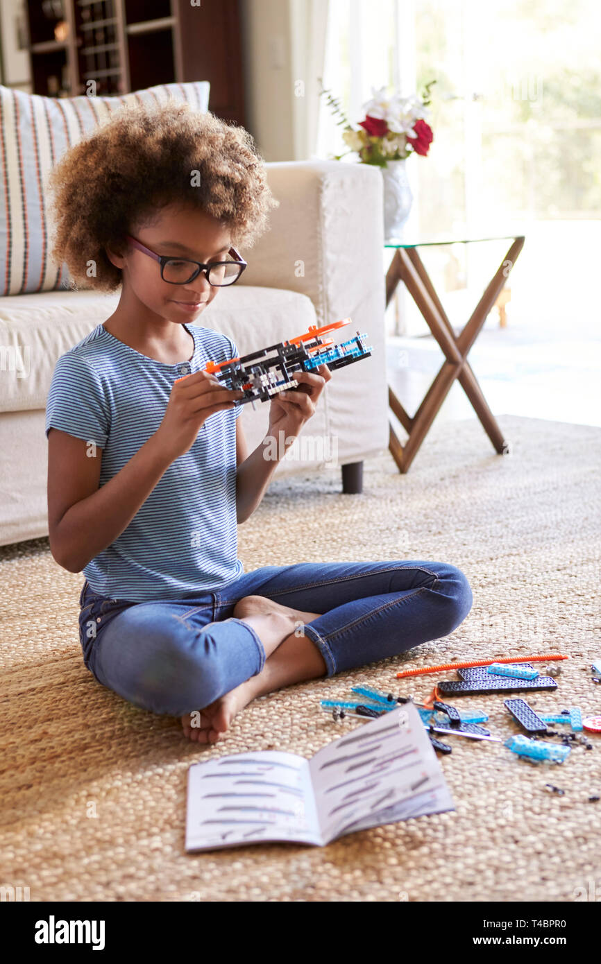 Pre-teen ragazza seduta sul pavimento del salotto la costruzione di un giocattolo da un kit di costruzione, close up, verticale Foto Stock