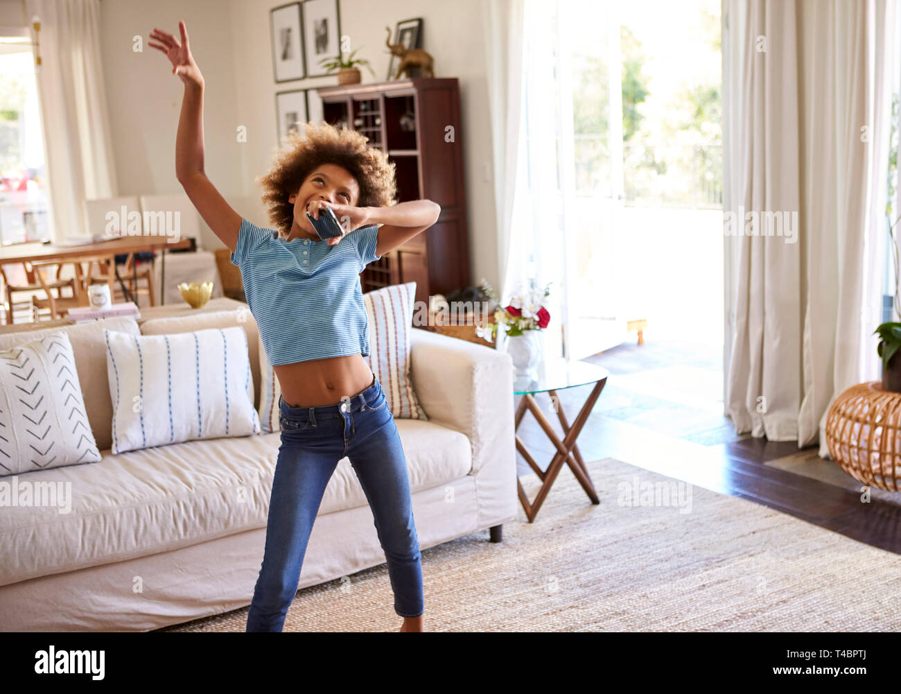 Pre-teen ragazza per ballare e cantare insieme alla musica nel salotto di casa utilizzando il suo telefono cellulare come un microfono, tre quarti di lunghezza Foto Stock