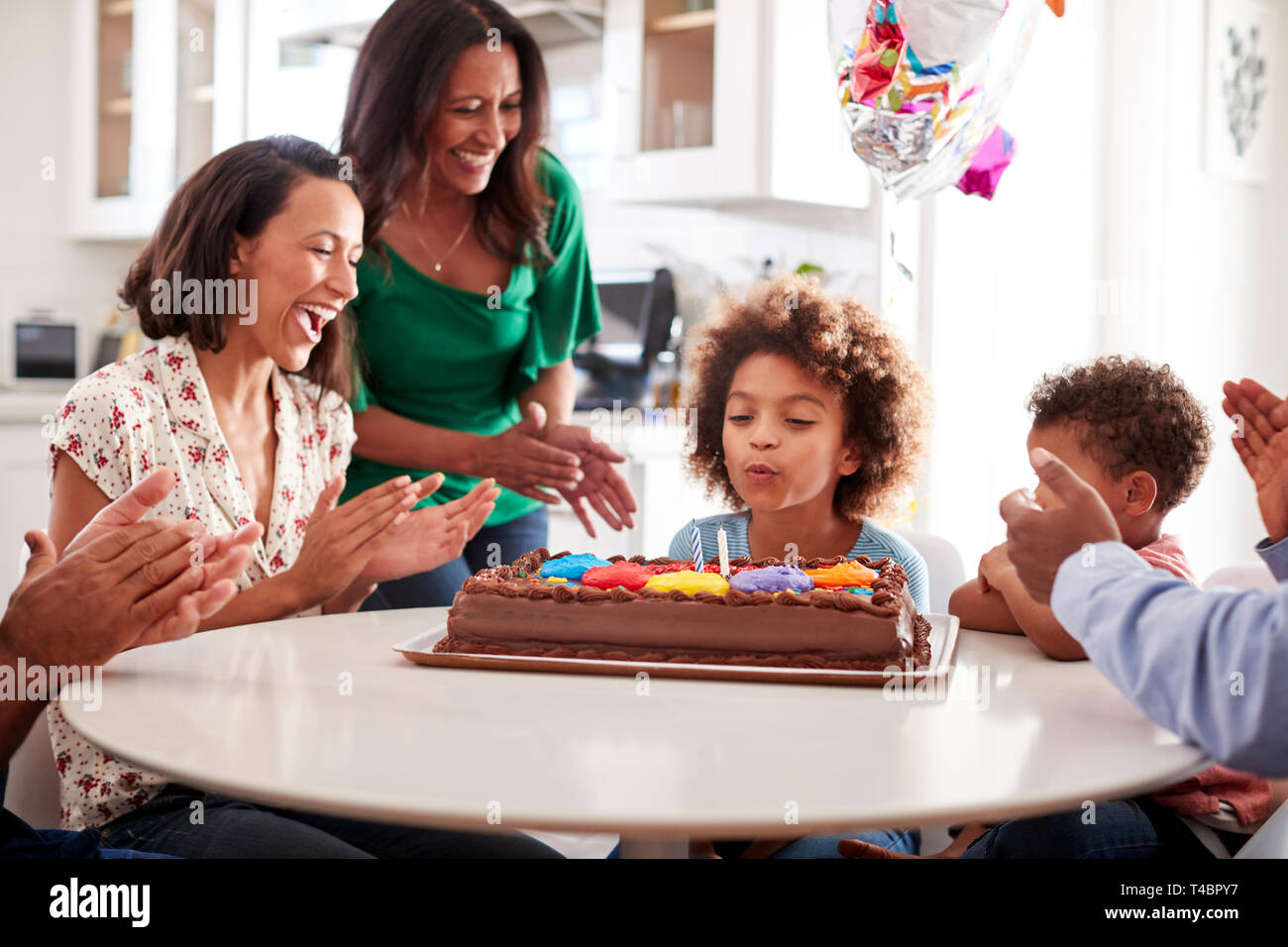 Pre-teen girl soffiando fuori le candeline sulla torta di compleanno seduti al tavolo in cucina con i suoi tre generazioni la famiglia, il fuoco selettivo Foto Stock