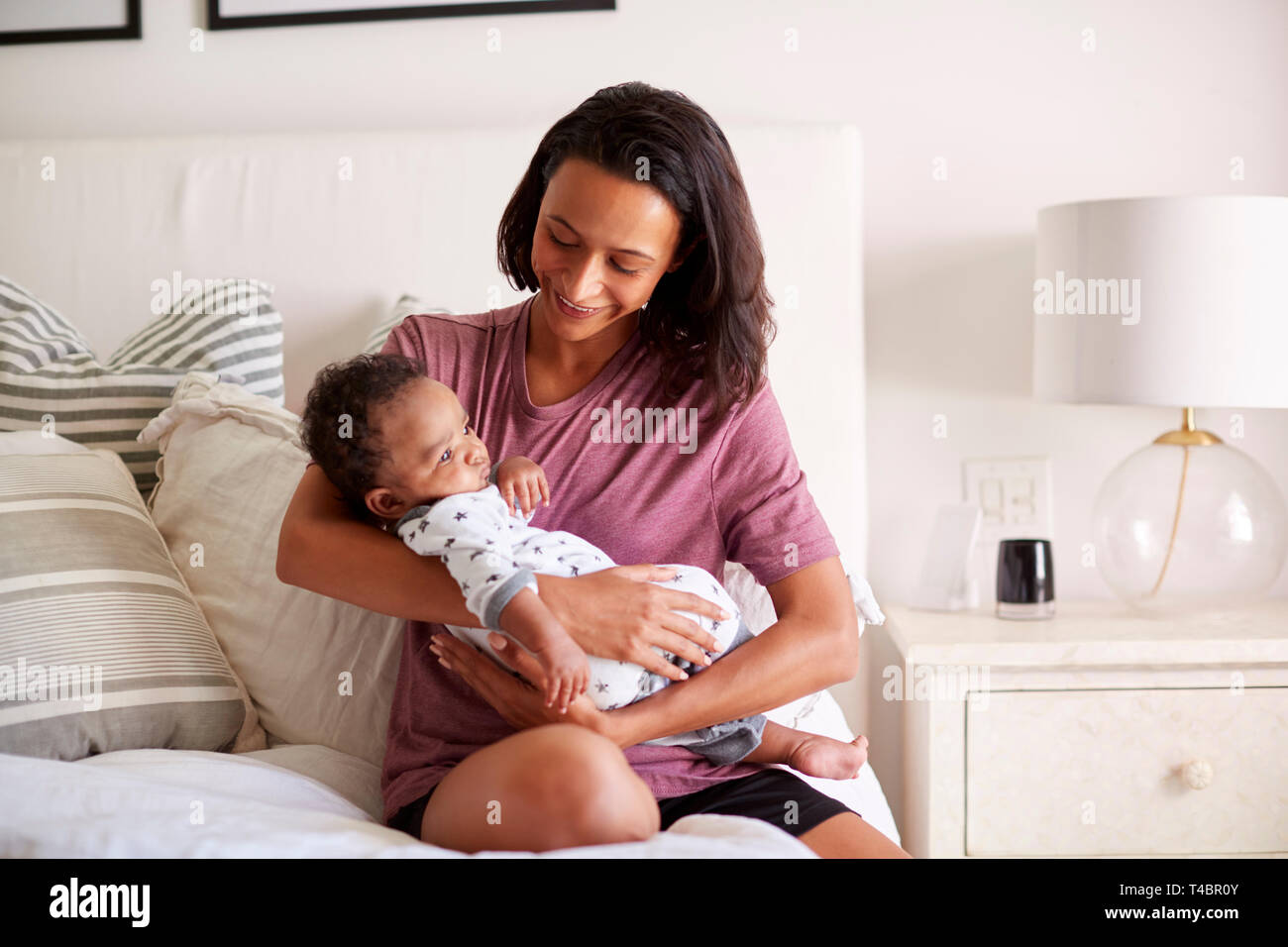 La millenaria razza mista madre seduta sul suo letto tenendo le sue tre mesi Figlio bambino nelle braccia Foto Stock