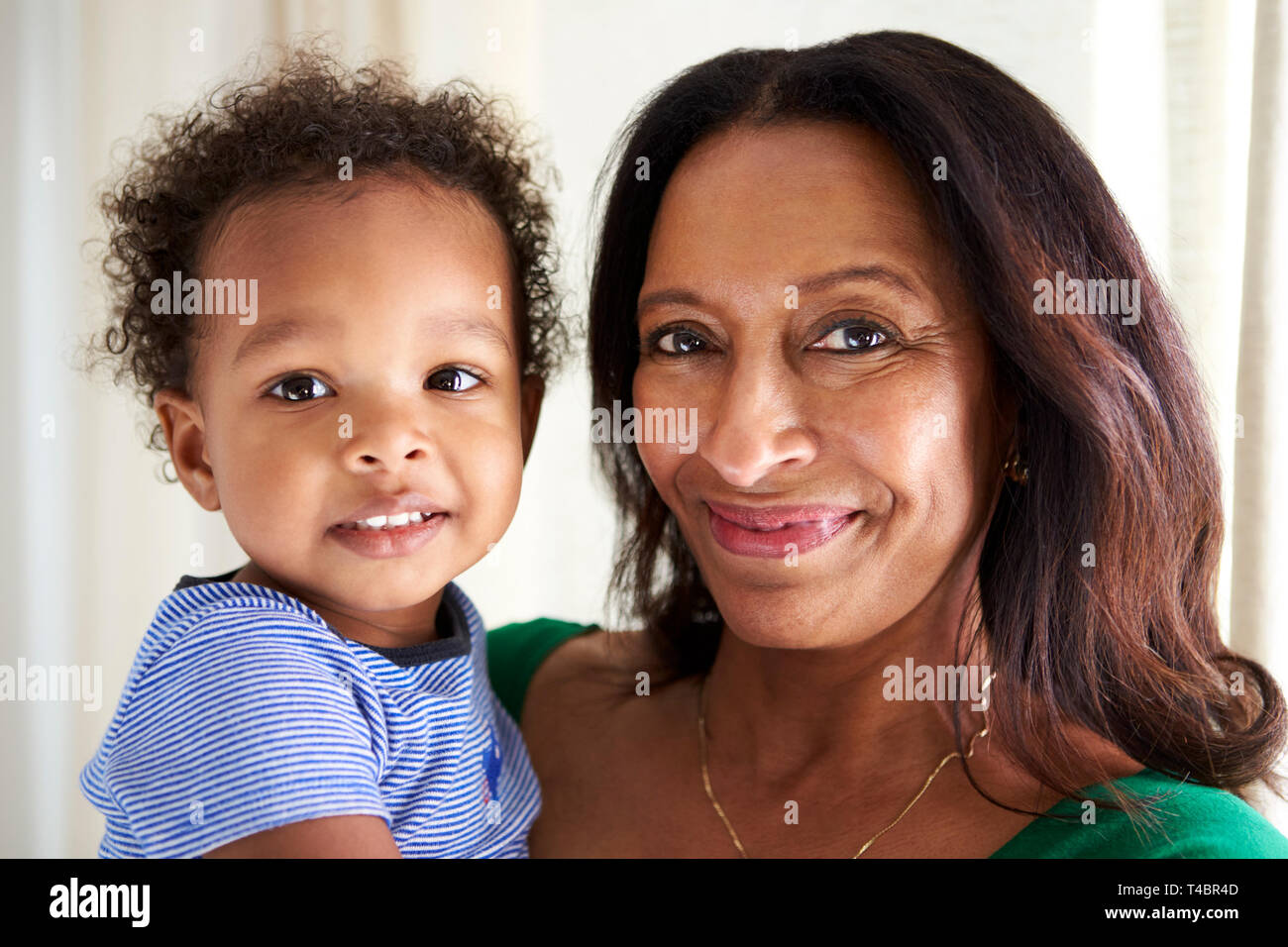 Felice razza mista di mezza età nonna tenendo i suoi due anni di nipote, sia cercando di fotocamera a sorridere, vicino, testa e spalle Foto Stock