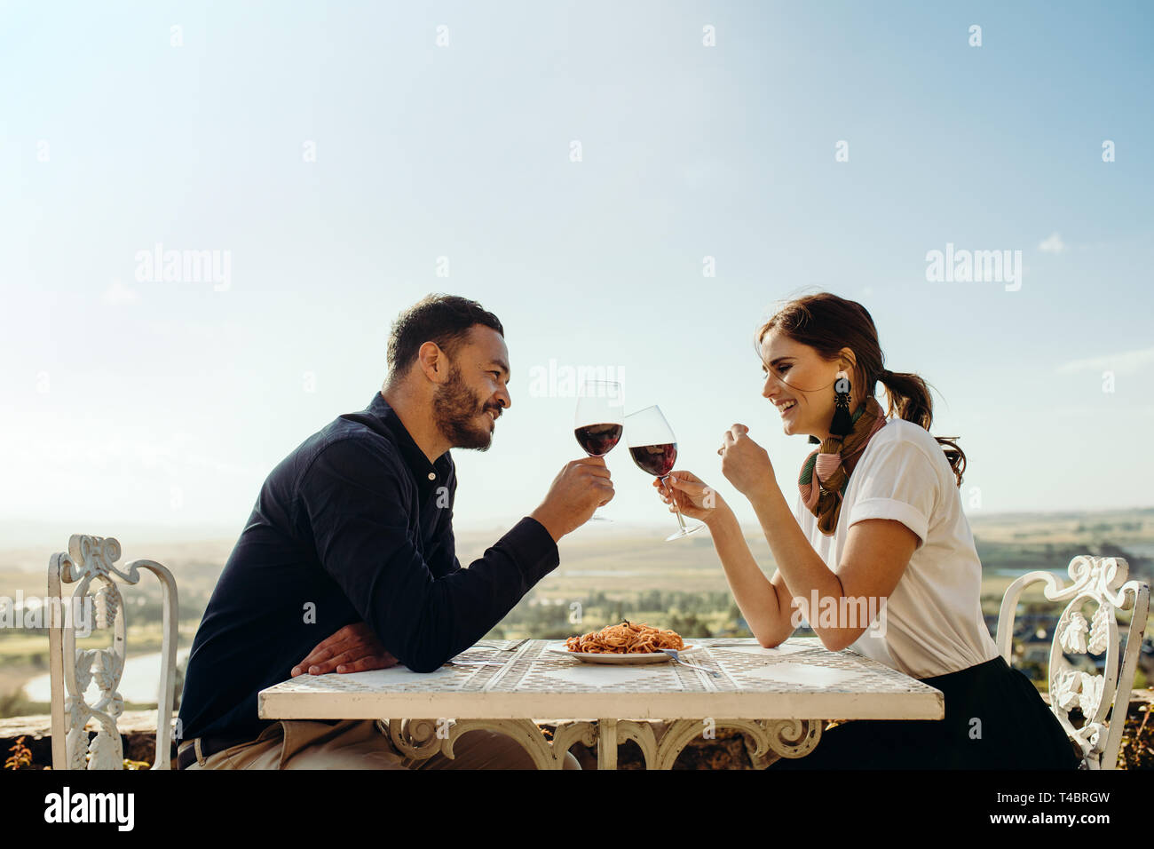 Sorridente giovane seduto in un ristorante Come tostare il bicchiere di vino rosso. Coppia felice su una data a parlare con ogni altra azienda bicchiere di vino. Foto Stock