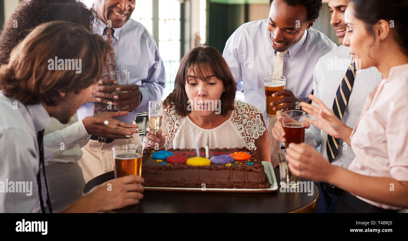 Imprenditrice soffiando le candeline sulla torta di compleanno alla celebrazione nel Bar con i colleghi Foto Stock