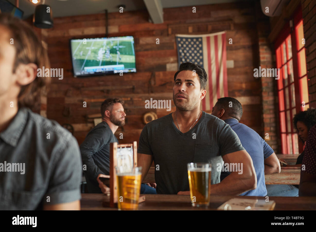 Amici maschi a bere birra e guardare la partita sullo schermo in Sports Bar Foto Stock