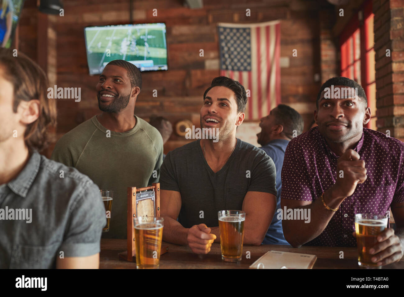 Amici maschi a bere birra e guardare la partita sullo schermo in Sports Bar Foto Stock