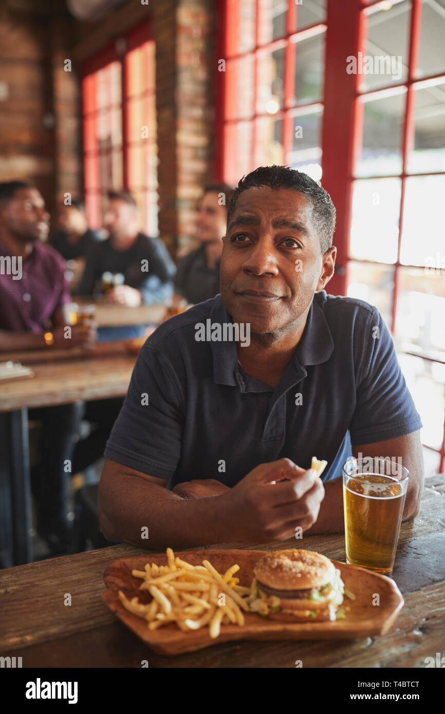 L'uomo la visione di gioco sullo schermo nel Bar Sport di mangiare hamburger e patatine fritte Foto Stock