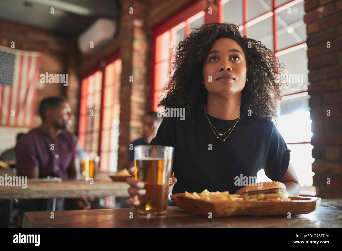 La donna la visione di gioco sullo schermo nel Bar Sport di mangiare hamburger e patatine fritte Foto Stock