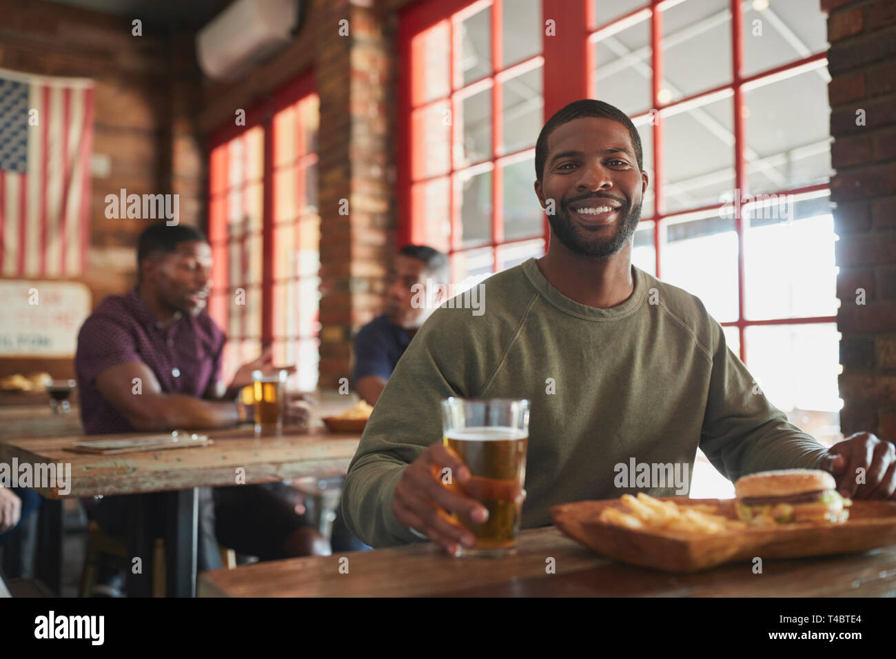 Ritratto di uomo nel Bar Sport di mangiare hamburger e patatine fritte Foto Stock