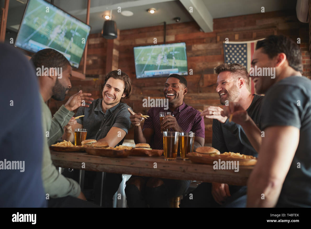 Amici maschi a bere birra e mangiare hamburger in Sports Bar Foto Stock