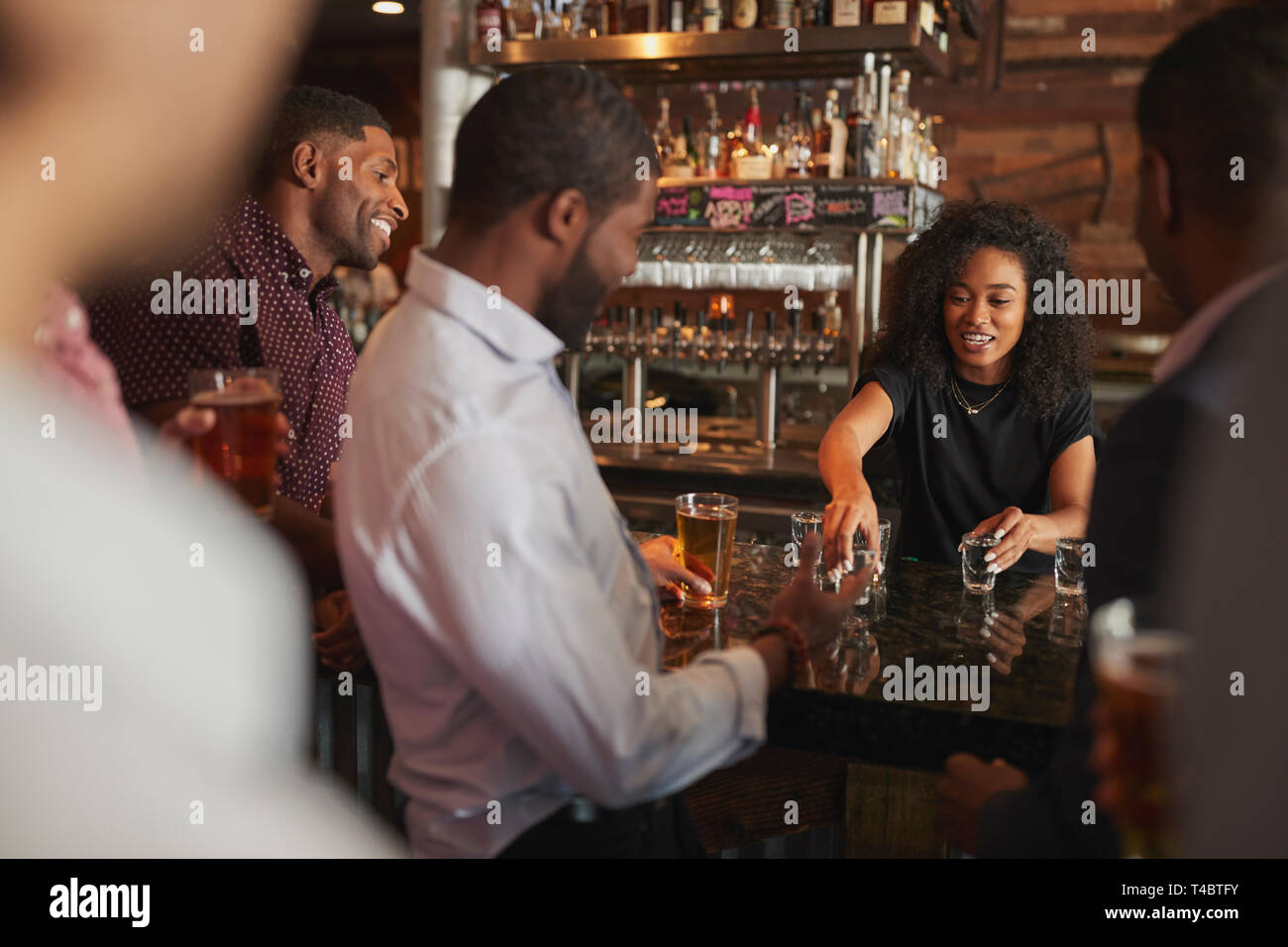 Barista serve scatti di gruppo di amici maschi sulla notte fuori in bar Foto Stock