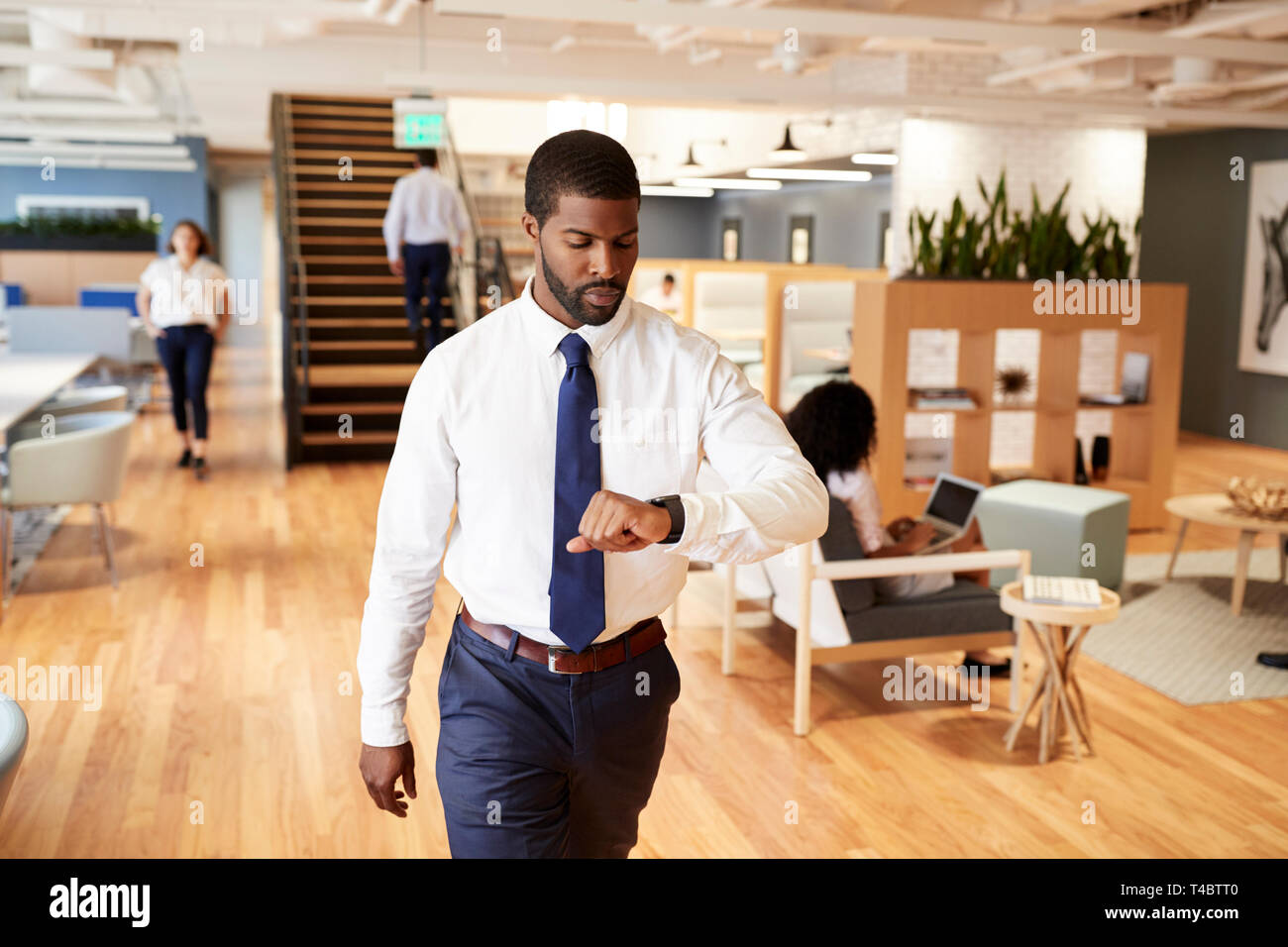 Imprenditore a piedi attraverso un ufficio moderno controllo Dati sanitari su Smart Watch Foto Stock