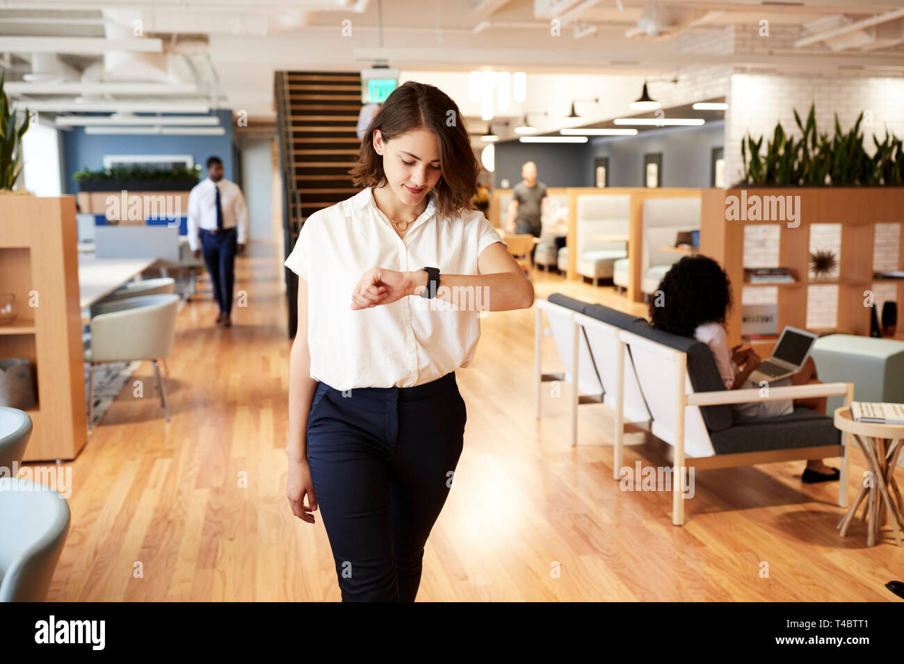 Imprenditrice a piedi attraverso un ufficio moderno controllo Dati sanitari su Smart Watch Foto Stock