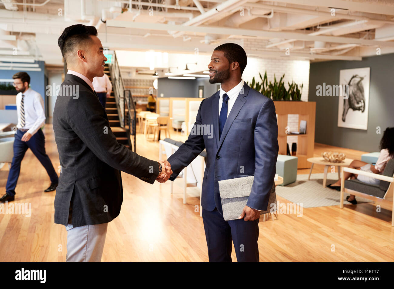 Due imprenditori incontro e stringono le mani in Modern Open Plan Office Foto Stock