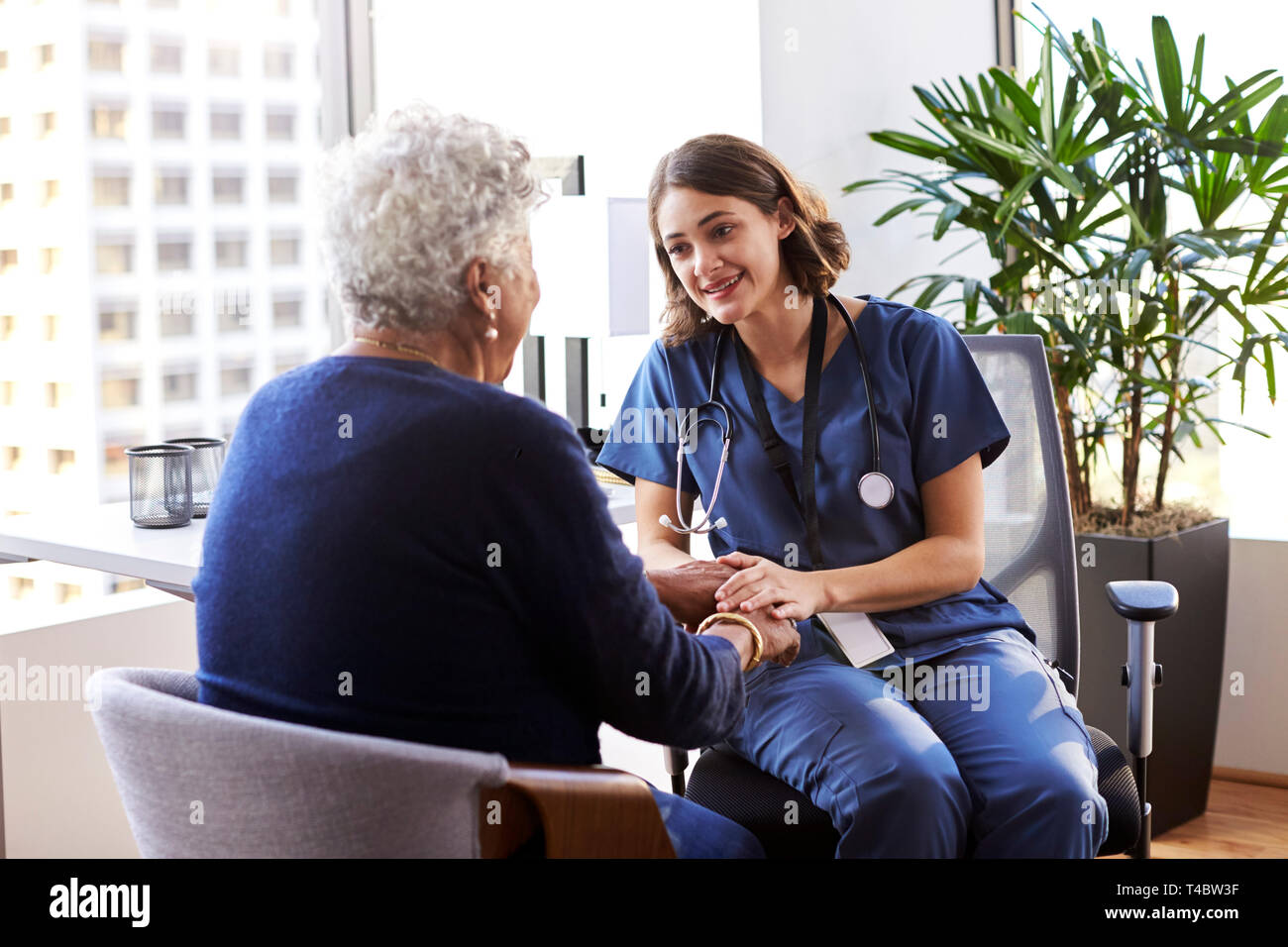 L'infermiera indossando Scrubs In ufficio rassicurante Senior paziente femmina e tenendo le Sue mani Foto Stock