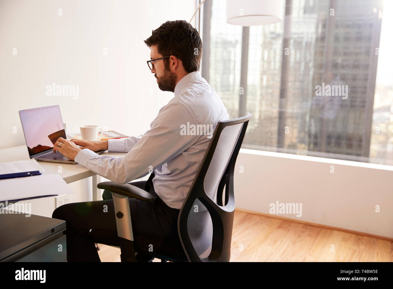 Imprenditore seduto alla scrivania che lavora sul computer portatile in ufficio moderno Foto Stock