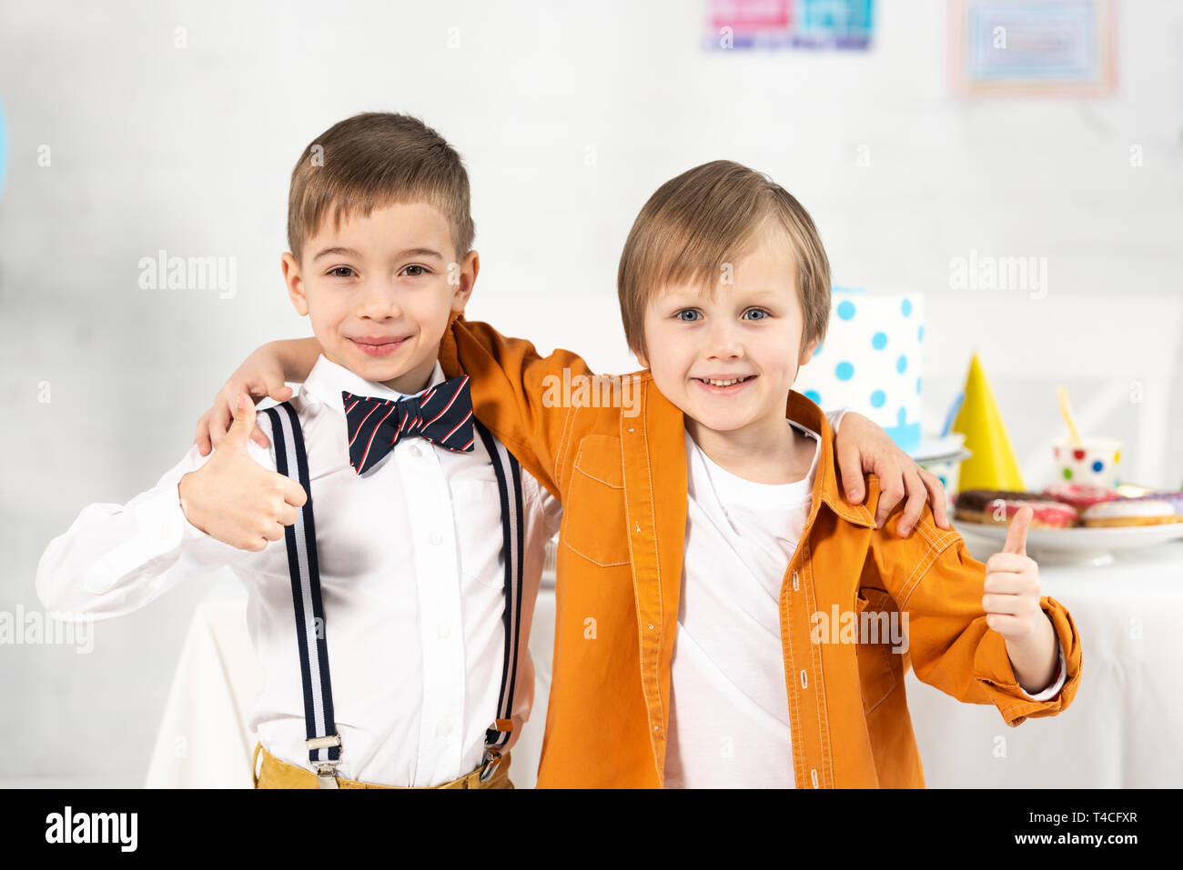 Adorabili preteen boys guardando la telecamera, avvolgente e mostrando pollice in alto durante la festa di compleanno Foto Stock