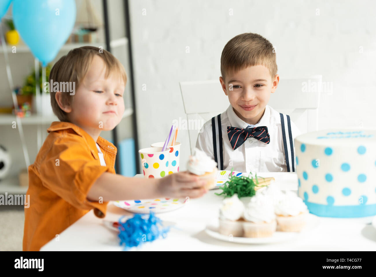 Adorabili preteen boys seduta a tavola con tortine durante la festa di compleanno Foto Stock